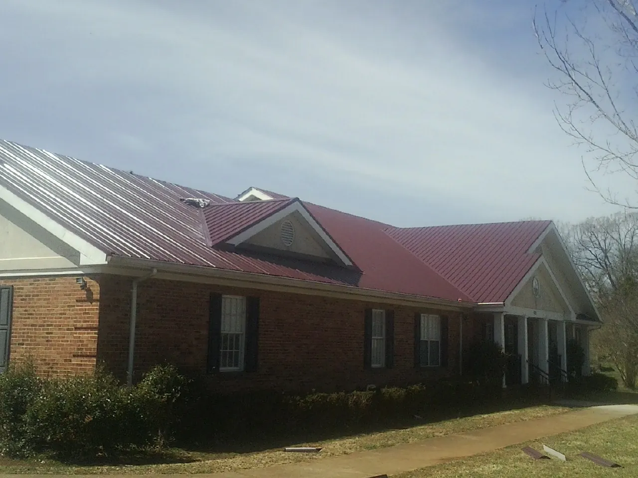 Red metal roof with gabled entries on a long brick building, from a Hail Damage Roof Repair job in Evans City