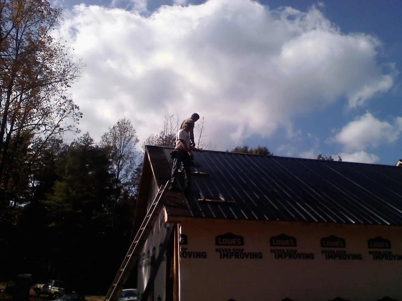 Roofer fastening dark metal panels high against a cloudy sky, from a Roof Inspection job in Evans City
