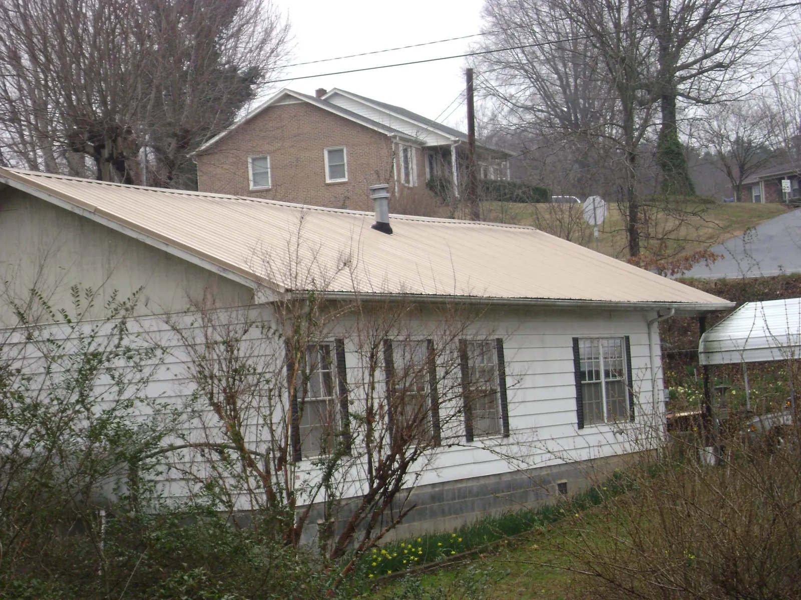 Tan metal roof on a white sided house set into a hillside — Commercial Roofing by Roofing Brothers in Evans City